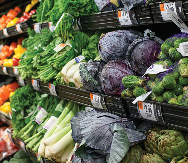 Exhibición colorida de vegetales, que incluye repollo morado, zanahorias y verduras de hoja verde en una tienda de comestibles o en un mercado agrícola.